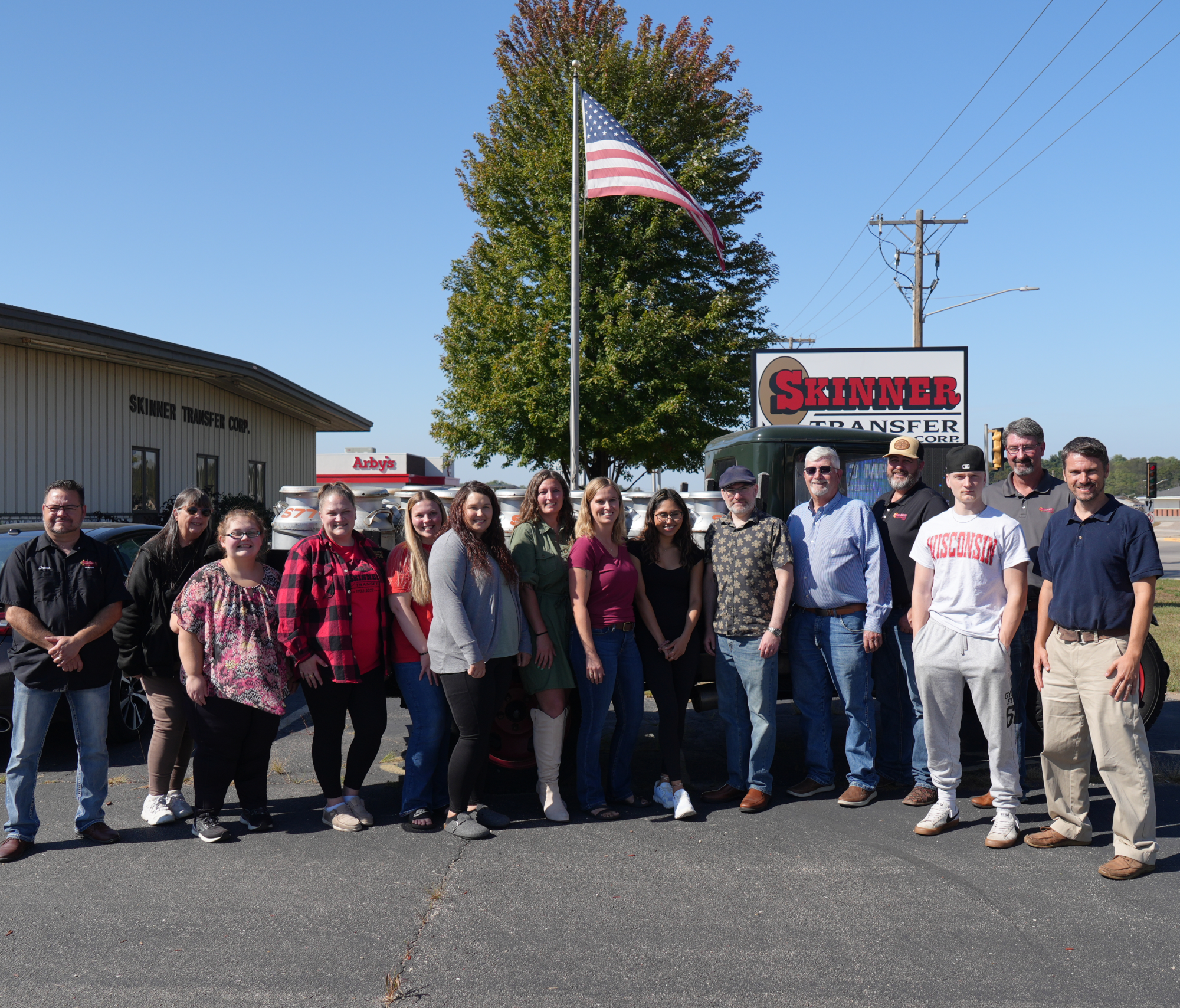 Group photo of Skinner Transfer employees and associates outside their facility, featuring an American flag and company signage.