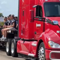 A vibrant red truck transports a group of people sitting on its trailer, celebrating during a parade or community event.